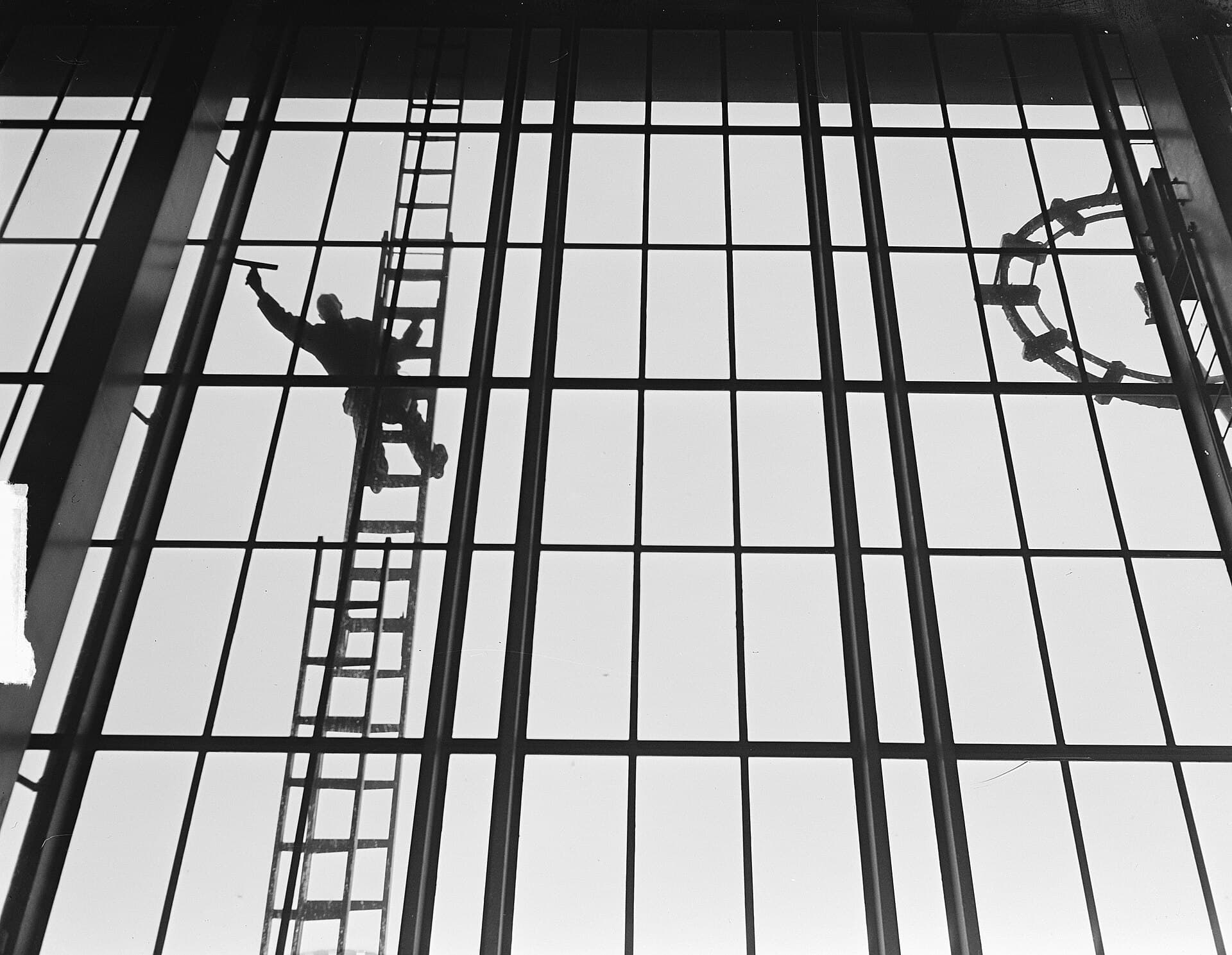 Silhouet van een glazenwasser op een ladder tegen een enorme glazen wand