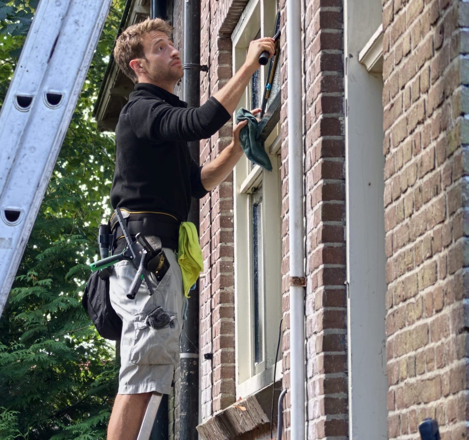 Glazenwasser op de ladder met wisser en gereedschapsriem